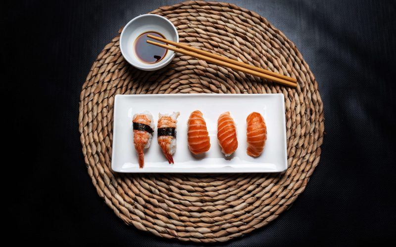 nigiri-sushi-white-ceramic-plate-with-chopsticks-bowl-with-soy-sauce-round-wicker-tablecloth-black-background